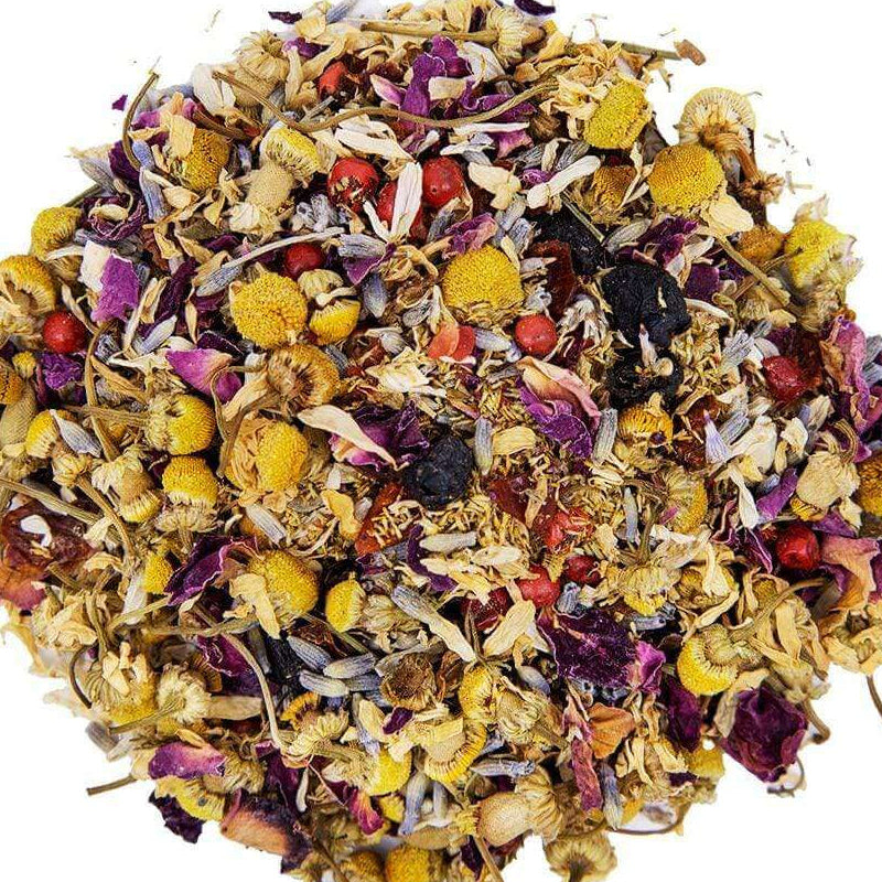 A circular pile of loose-leaf herbal tea blend featuring dried yellow chamomile flowers, purple rose petals, and small red berries on a solid white background.