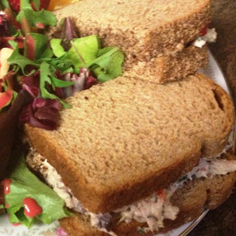 A close-up of a sandwich made with brown whole wheat bread and filled with a creamy chicken salad, served on a plate with a side salad.